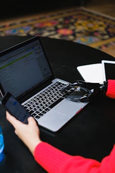 Close-up of a person with a prosthetic hand typing on a laptop while holding a phone, showcasing modern technology.