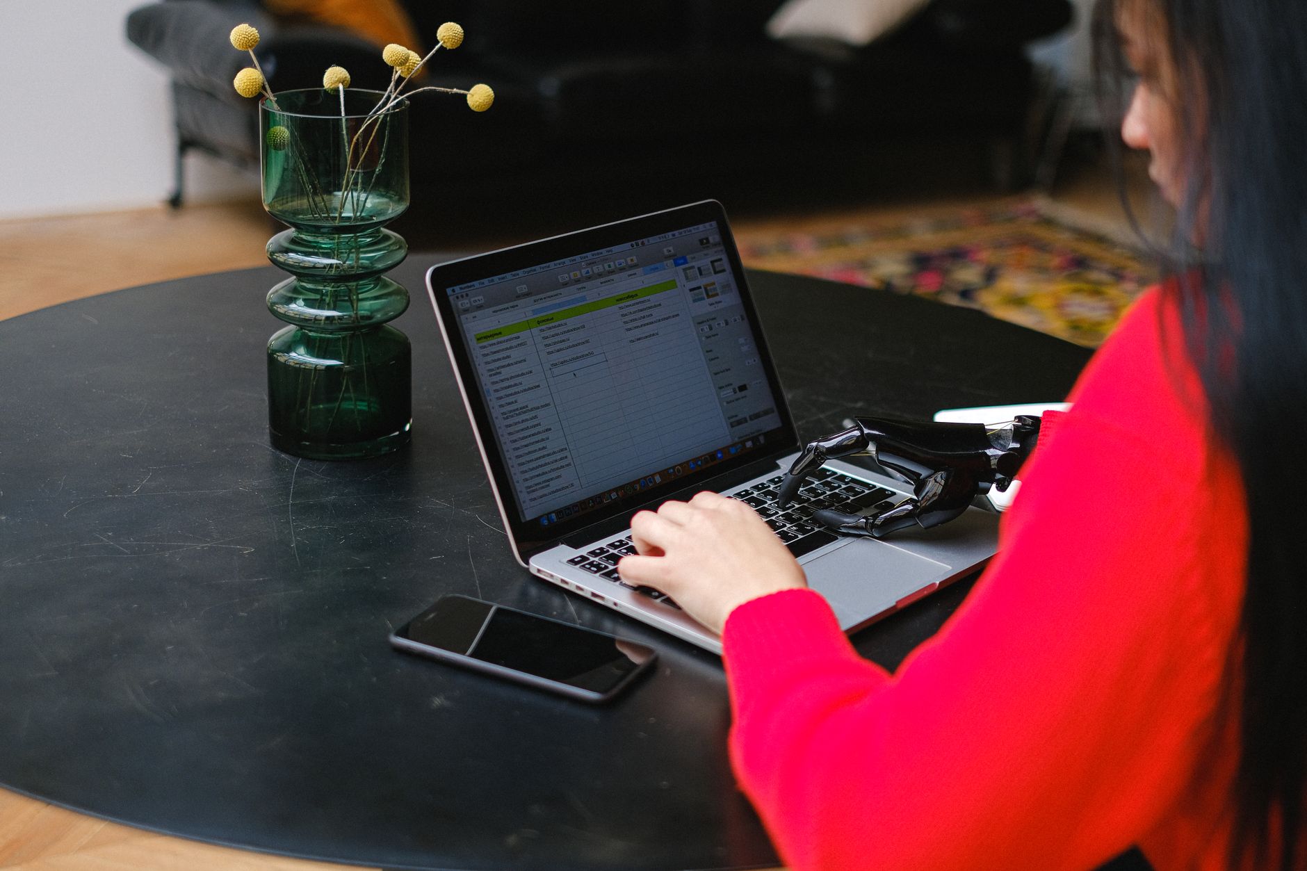 A woman with a prosthetic hand typing on a laptop at a sleek indoor table.
