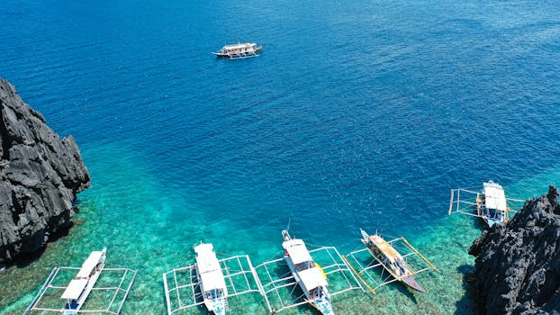 Aerial shot of traditional boats on crystal-clear waters near rocky coastline in the Philippines, epitomizing tropical paradise.