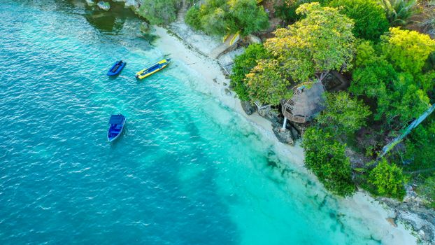 Drone view of calm blue ocean water with bright boats and beach with green tropical plants