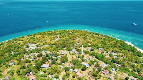Aerial view of calm blue sea water near shore with green exotic plants and small buildings