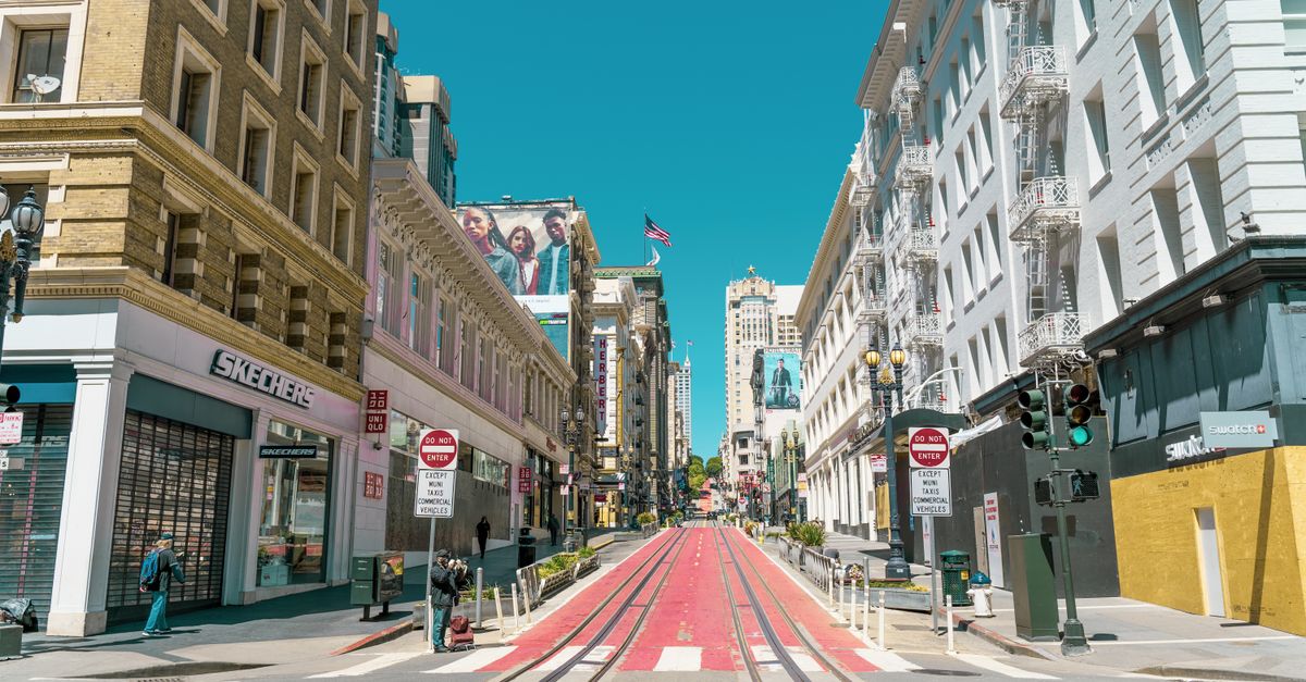 Empty road with sidewalks and traffic lights and signs located between downtown buildings