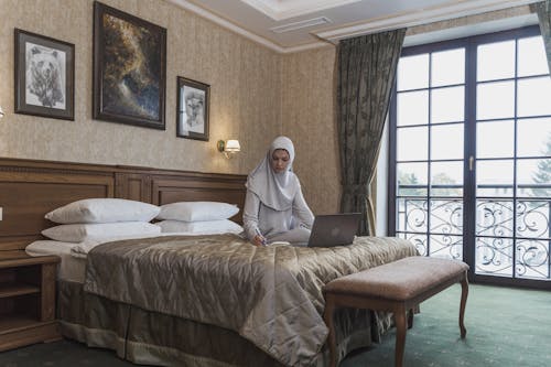 Woman in White Hijab Sitting on Bed Using Macbook