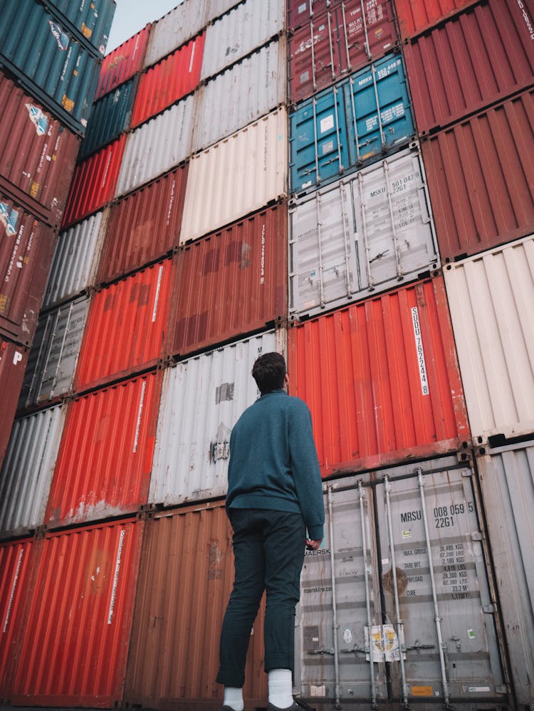 Man In Blue Dress Shirt Looking At A Stack Of Cargo Containers