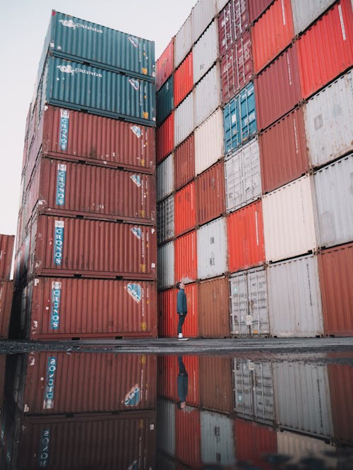A Man Standing Near a Pile of Red and Blue Intermodal Containers