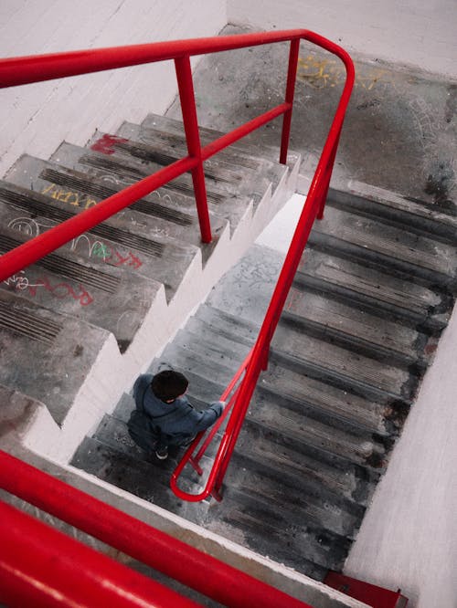 Man Holding To A Red Handrail While Going Down The Stairs 
