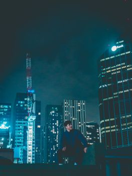 夜晚的墨尔本，一名年轻人坐在灯光明亮的摩天大楼前