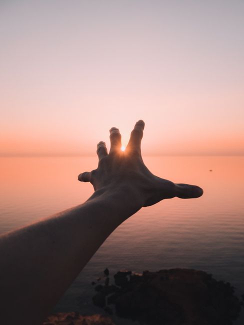 A silhouette of a hand reaching towards the setting sun over a tranquil ocean at Black Rock, Australia.