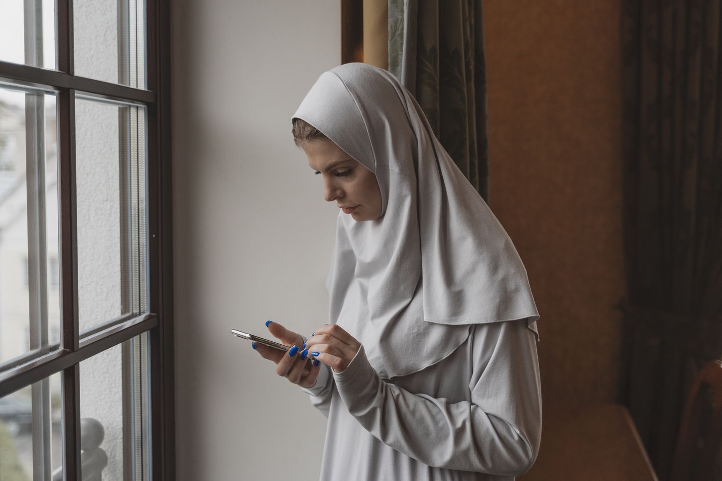 Woman in a headscarf using a smartphone by a window
