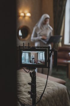 Muslim woman in hijab setting up camera indoors for content creation, showcasing creativity and technology.