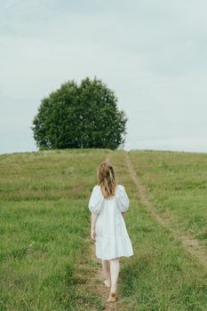 一名身穿白裙的女子赤脚走向草地上的大树