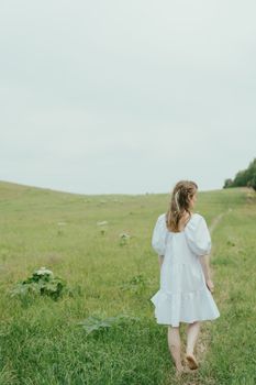 一位身穿白裙的女子赤脚走在宁静的夏季草地上