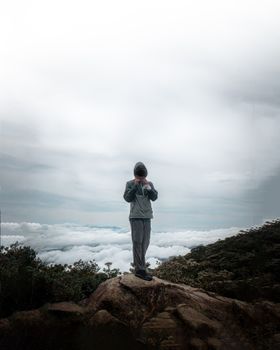 在马来西亚沙巴的拉瑙，一名孤独的徒步旅行者站在云海缭绕的山巅，捕捉着宁静的美景