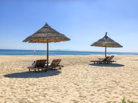 Peaceful sandy beach with thatched umbrellas and wooden loungers by the sea.