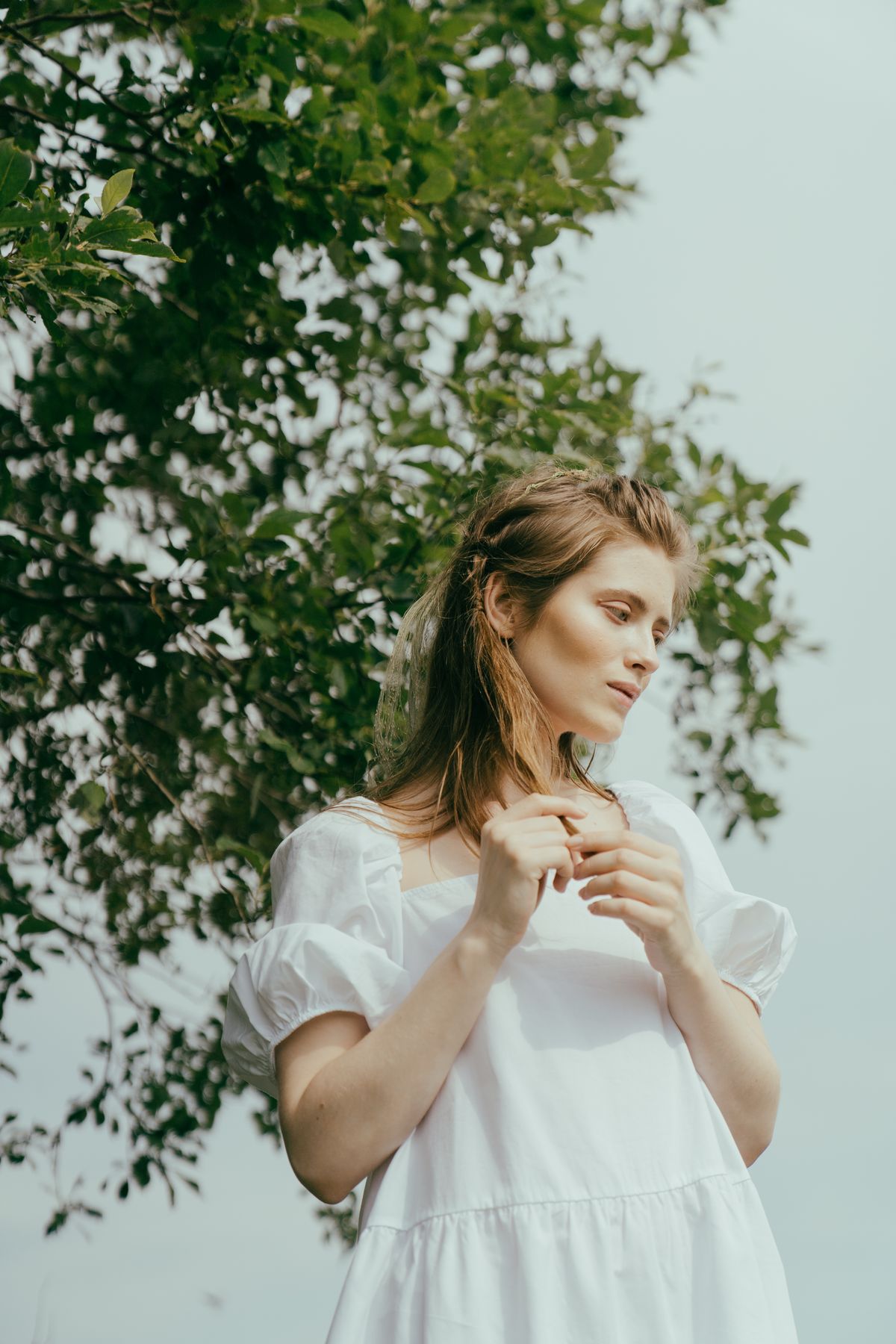 A woman in white standing beside a tree in soft natural light