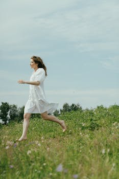 晴朗的天空下，一位穿着白色连衣裙的女人赤脚快乐地跑过绿色的草地