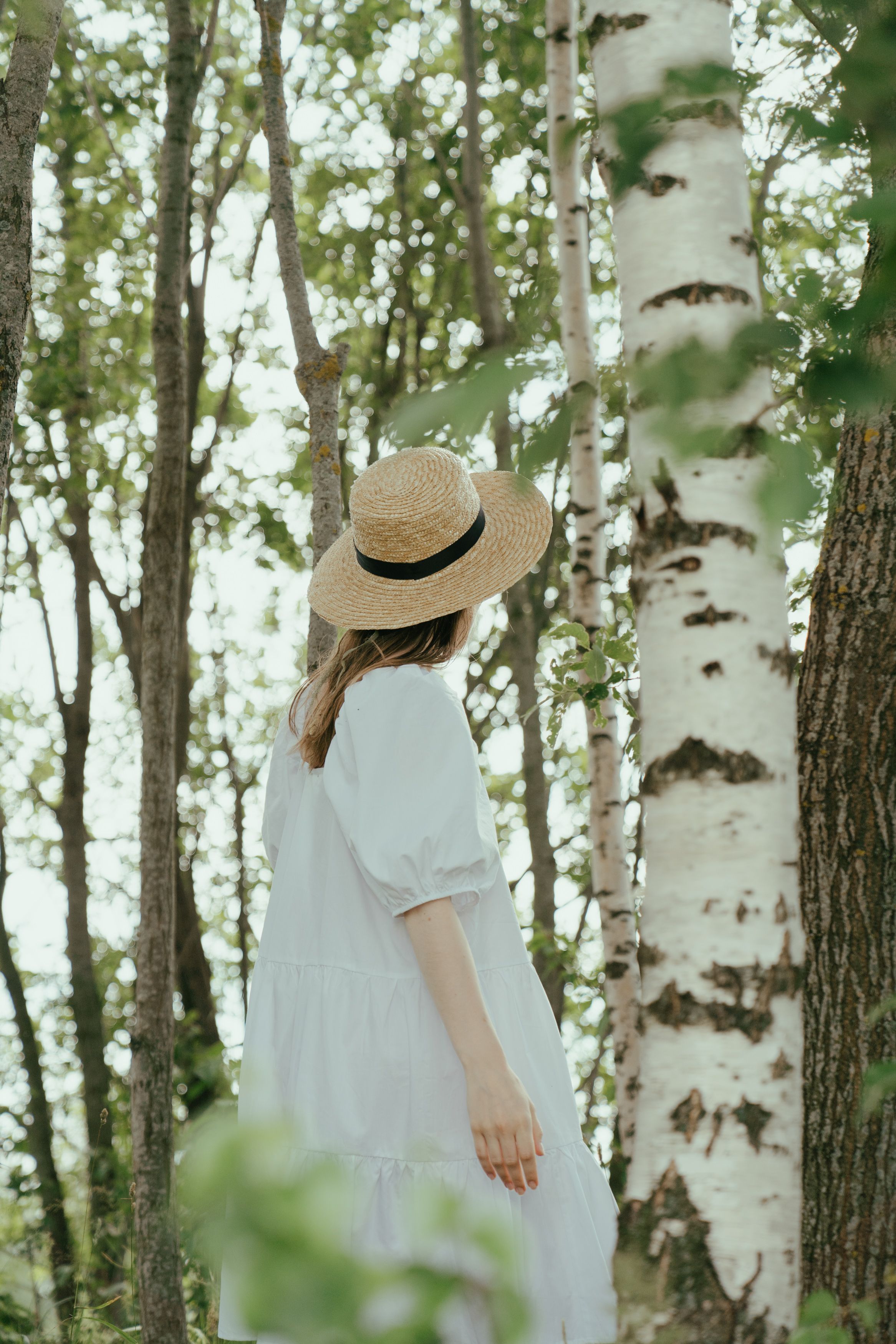 一个戴着草帽、身穿白色连衣裙的女人在森林里安静地散步