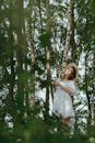 一个穿着白色连衣裙的女人，在高大的树木中微笑，在夏天享受宁静的森林