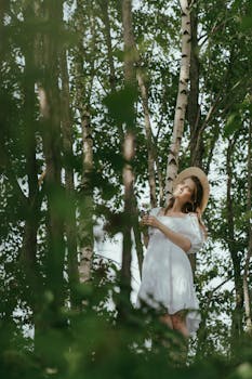 一名身穿白裙的女子，在高大的树木间微笑，享受着夏日森林的宁静