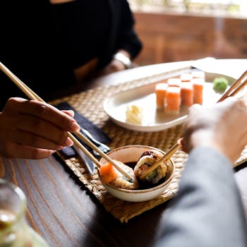 Two people sharing sushi using chopsticks, highlighting Japanese dining culture.