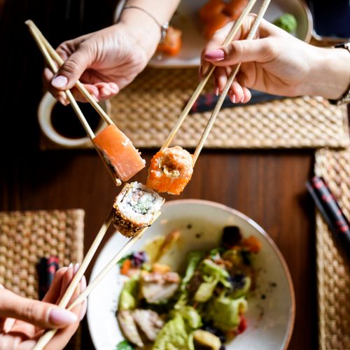 Free Hands holding sushi with chopsticks over a dining table setting. Perfect for food and dining themes. Stock Photo