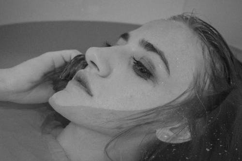 Black and white of stressful female resting in bathtub with clean transparent water