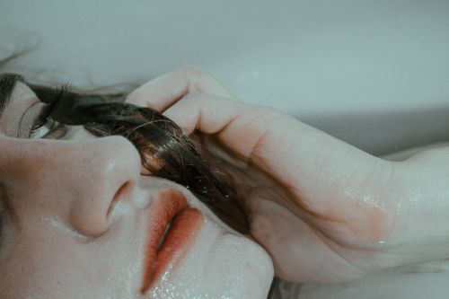 Free From above of sad female touching hair and looking away on bathtub with water Stock Photo