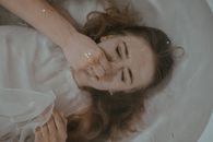 Top view of young upset female in white dress holding nose while lying under water in bathtub