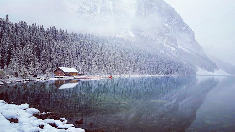 Wooden Cabin On The Bank Of A River In Mountains In Winter