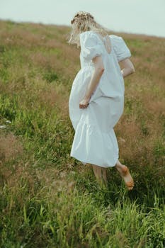 一名赤脚的妇女穿着白裙子，走过郁郁葱葱的绿色草地