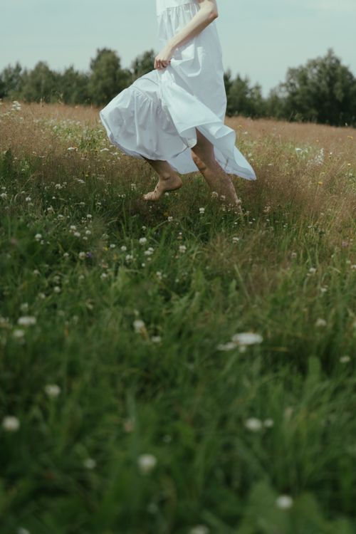Free A woman in a white dress runs joyfully through a blooming summer meadow. Stock Photo