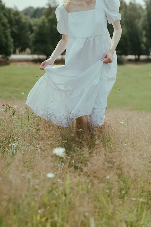 Woman in White Dress Walking on Green Grass Field