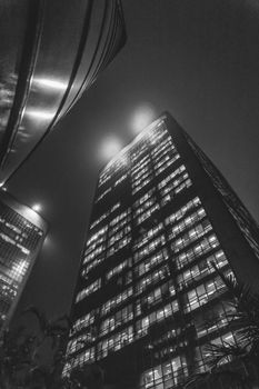 低角度视角下的现代摩天大楼，在夜间单色城市景观中显得格外明亮