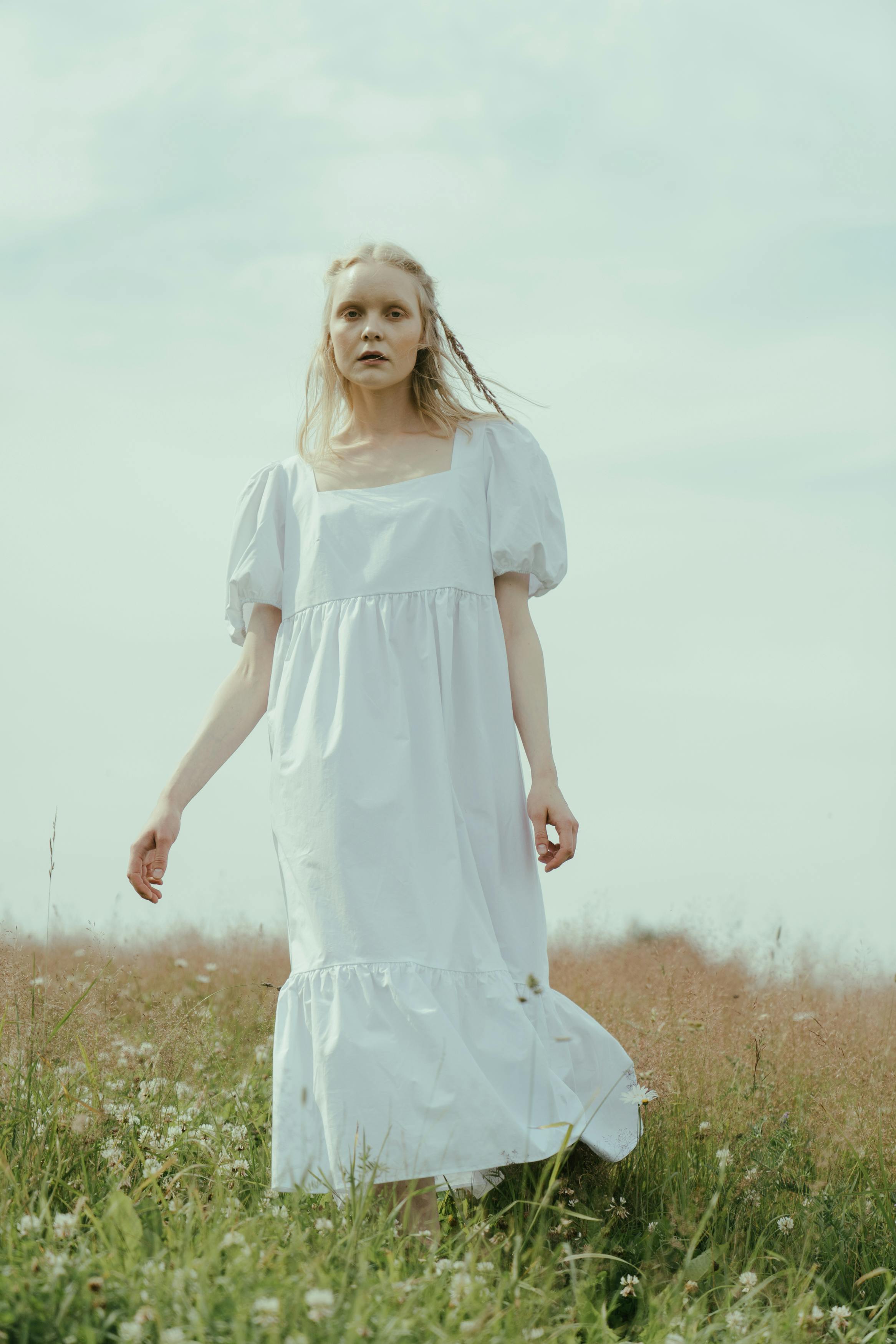 一名女子身穿飘逸白裙，安静地站在郁郁葱葱的草地上