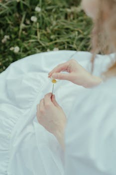 宁静的图像中，一个女人在长满草的草地上，轻轻拿着一朵洋地黄花