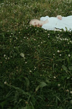 一位身着白裙的女子，躺在绿草如茵的草地上，四周点缀着小花