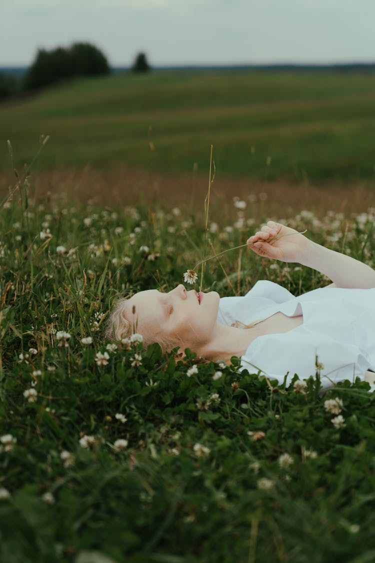 A Woman Smelling A Flower While Lying Down On A Field