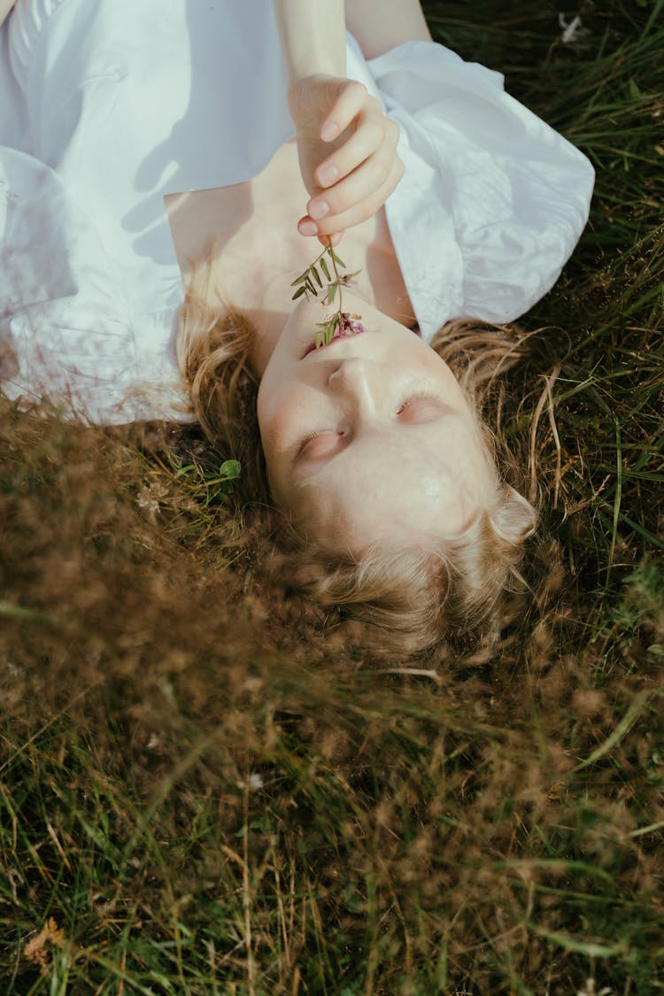 Woman In White Dress Lying On Green Grass Eating Plant