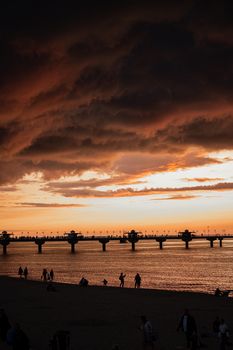 A stunning sunset over a pier in Miedzyzdroje, Poland, with silhouettes of people and dark clouds.