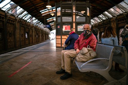 Free Man in a mask sitting on a bench at an indoor train station, waiting for transportation. Stock Photo
