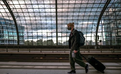 Free A person with a mask in a railway station, pulling luggage and embracing urban travel life. Stock Photo