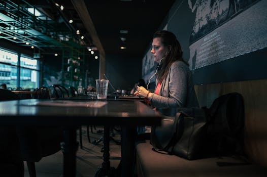 Focused woman using laptop with headphones in a cozy café setting.