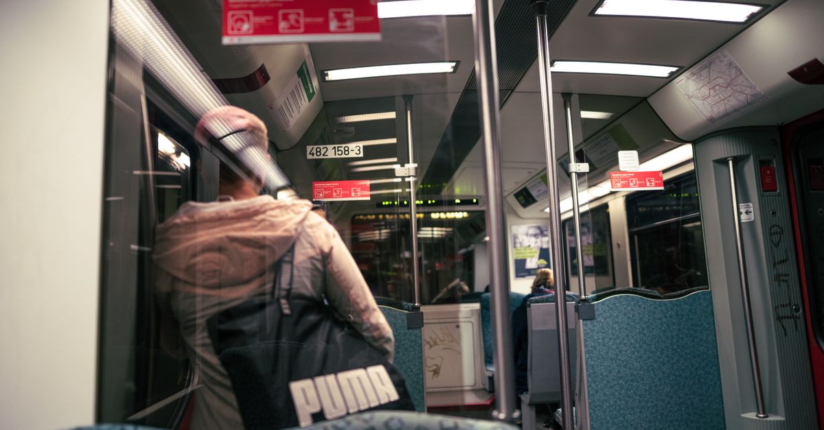 A person stands inside a modern subway train, reflected in the glass door.