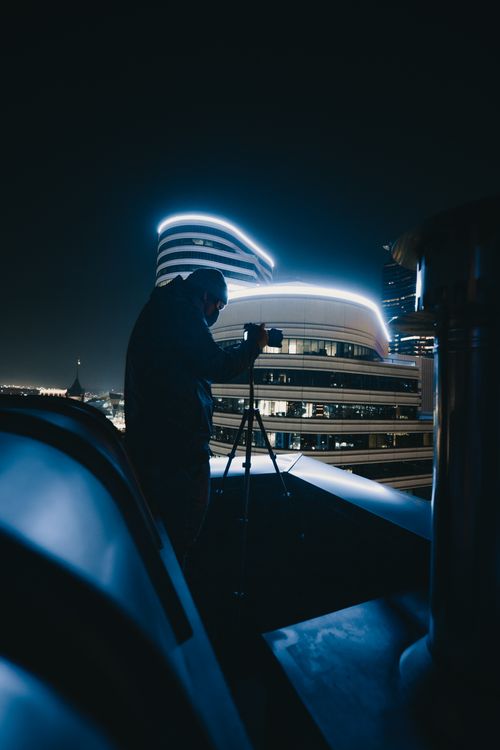 Free Silhouette of a photographer with a tripod shooting city lights at night. Stock Photo