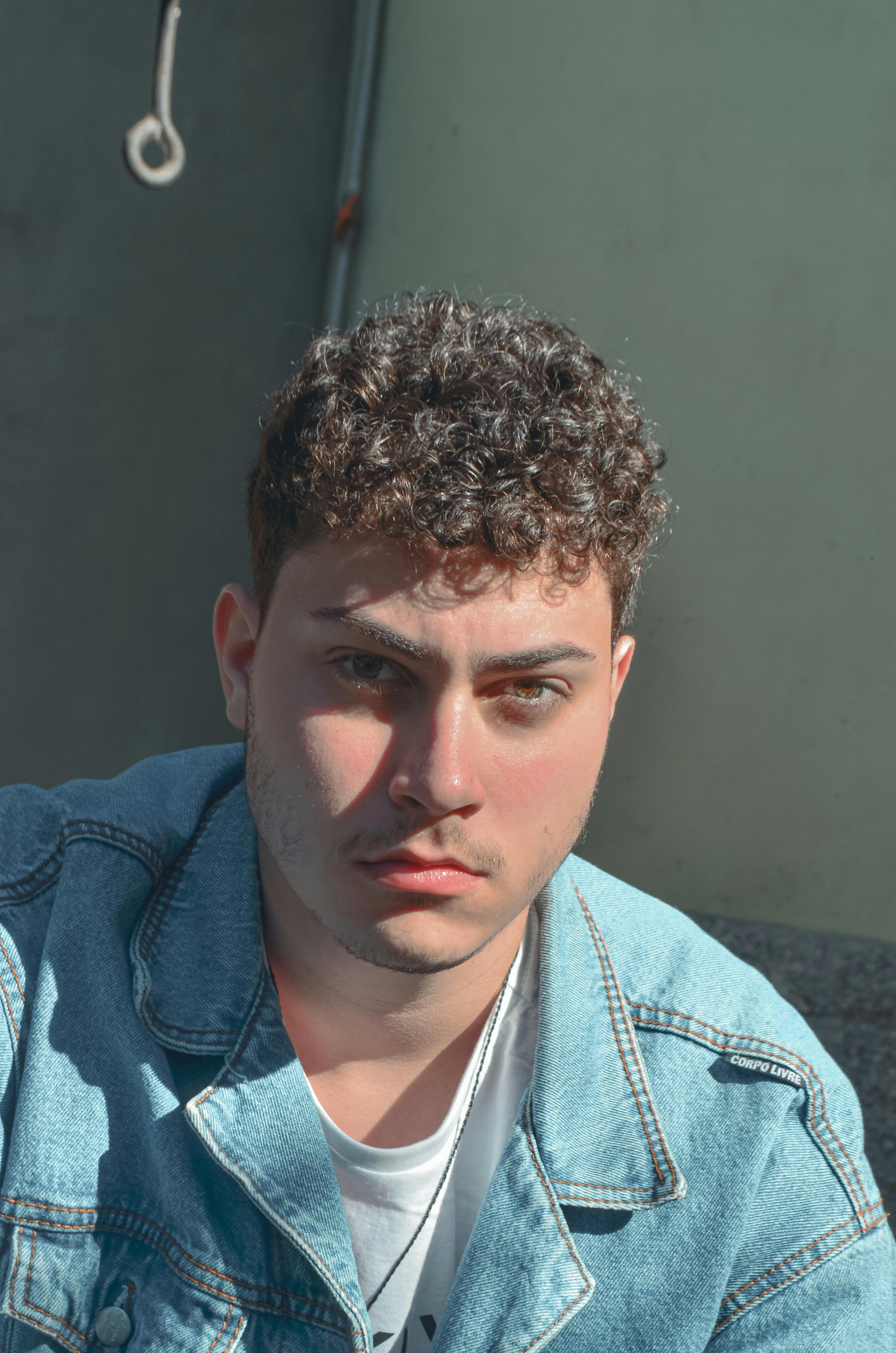 Portrait of a stylish young man wearing a denim jacket, outdoors in sunlight.