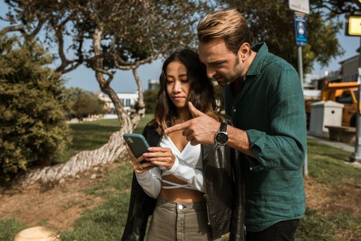 A man and woman using a smartphone together in a city park during daytime.