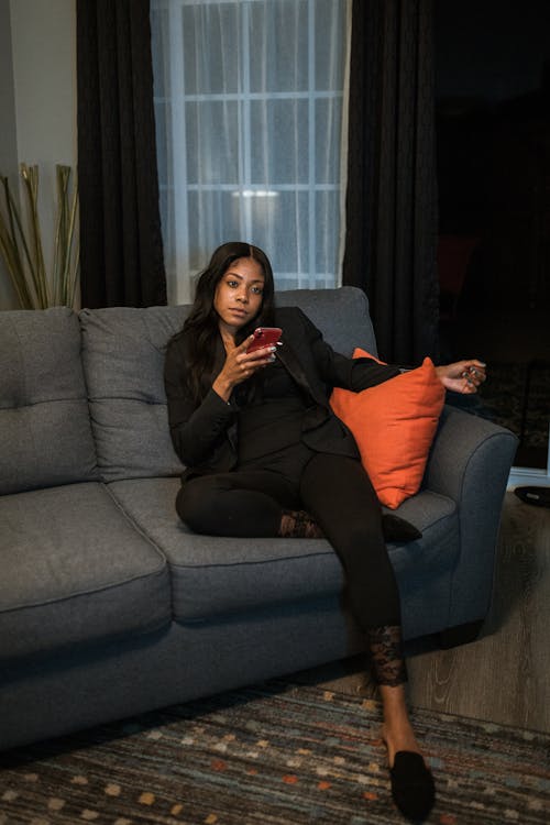 Free Woman Sitting on a Couch While Holding Her Iphone 11  Stock Photo