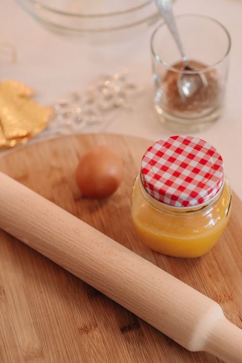 Free Warm kitchen scene with rolling pin, egg, and a jar of yellow liquid on wooden board. Stock Photo