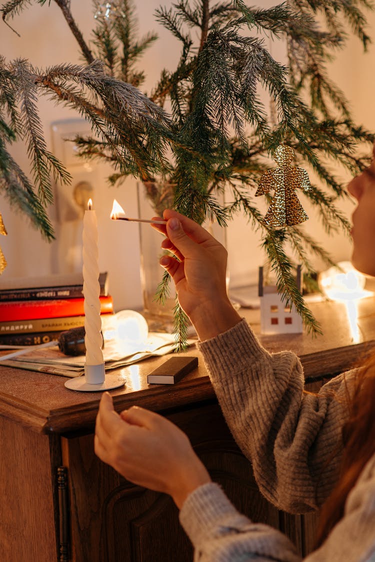 A Woman In A Sweater Lighting A Candle