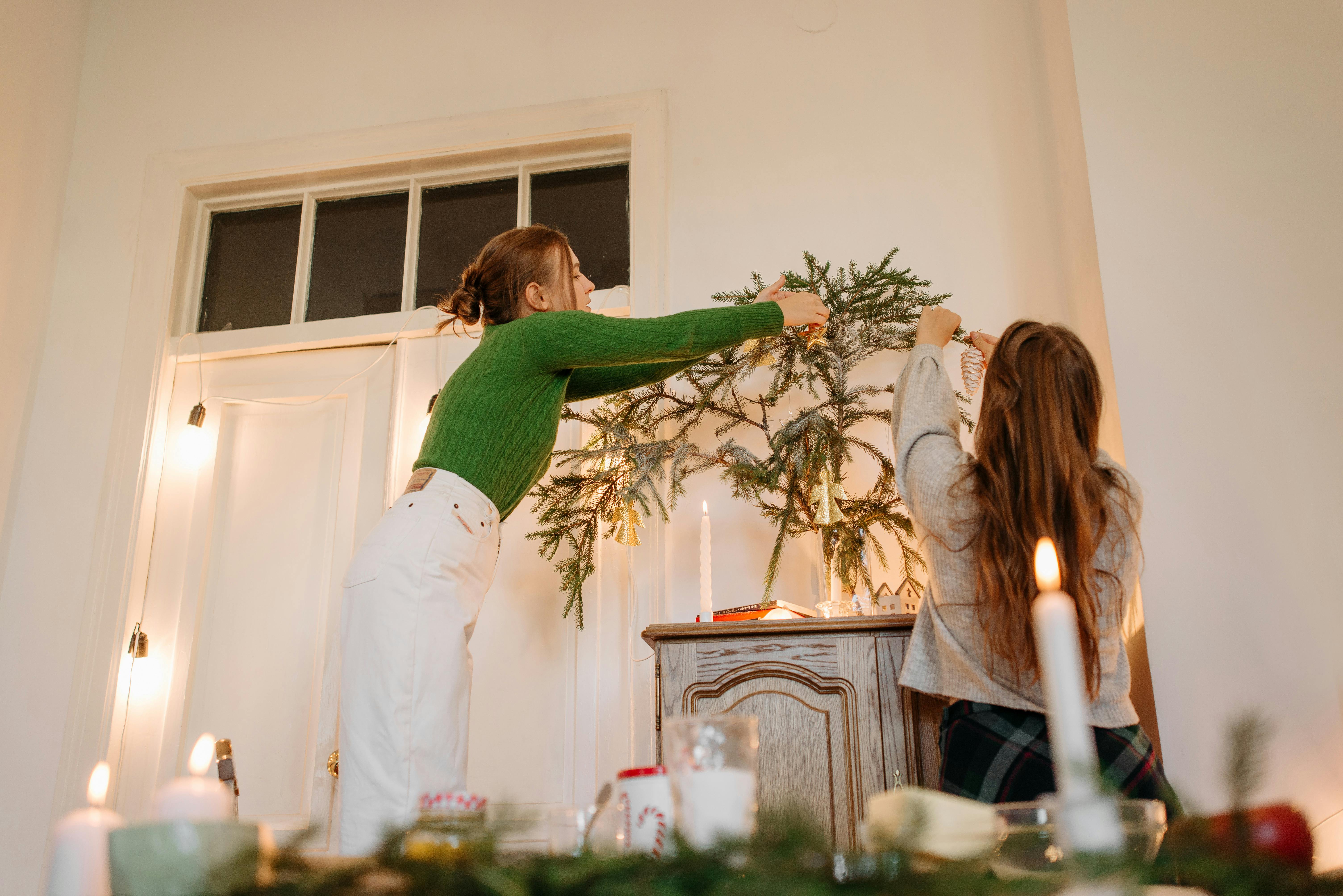 两名妇女用云杉树枝和蜡烛装饰房间，营造出室内的圣诞节日气氛
